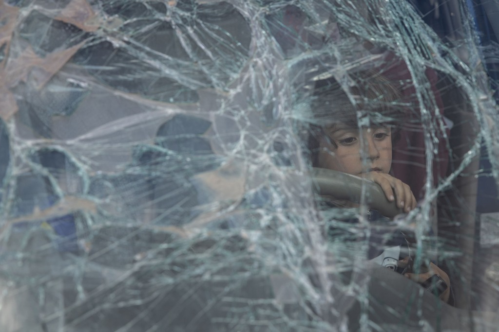 Chłopiec z Mariupola spogląda przez rozbitą przednią szybę rodzinnego samochodu