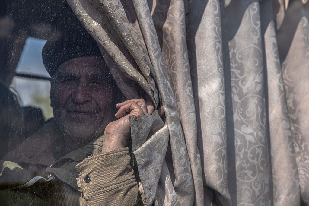 Starszy mężczyzna patrzy na niego, gdy siedzi w autobusie po przybyciu z frontowego miasta Urekiev, w punkcie ewakuacyjnym w Zaporożu na Ukrainie