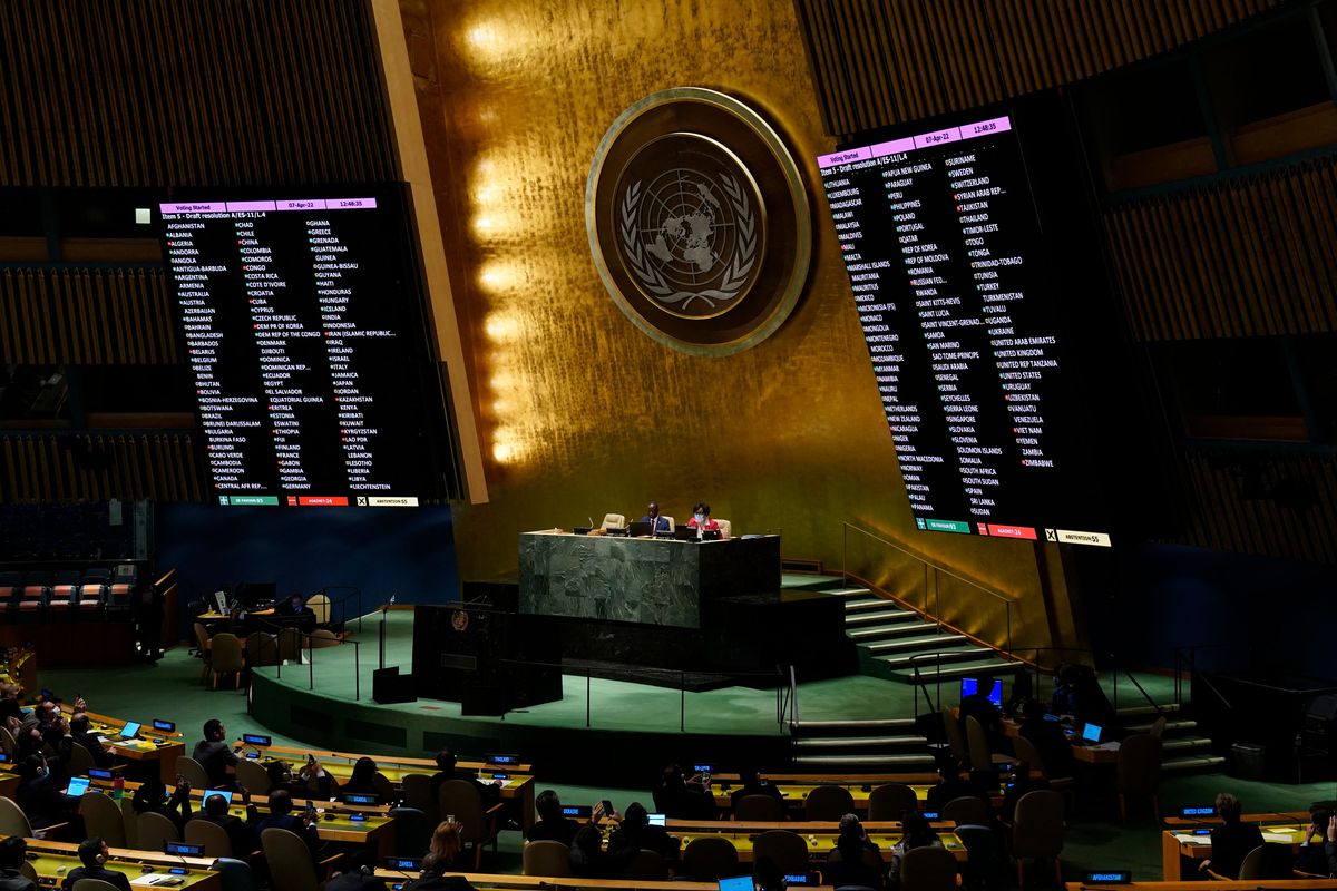 Large black screens perched above the crowds showing white text as the United Nations votes to remove Russia from the Human Rights Council.